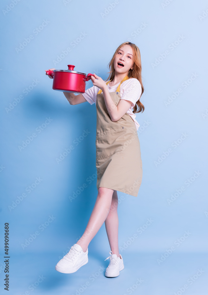 Image of young Asian woman holding pot on blue background