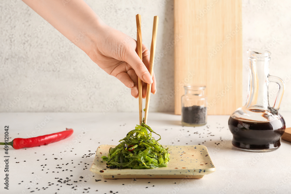 女人用筷子在浅色背景下吃健康的海藻沙拉