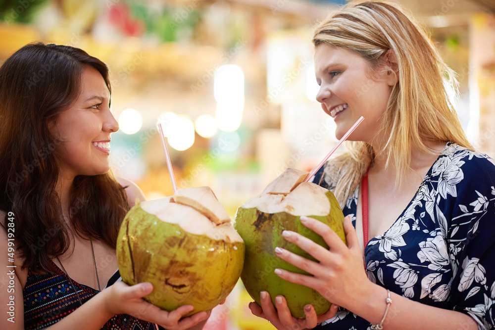 三人行。两名年轻女子在外国杂货店喝椰子的裁剪镜头