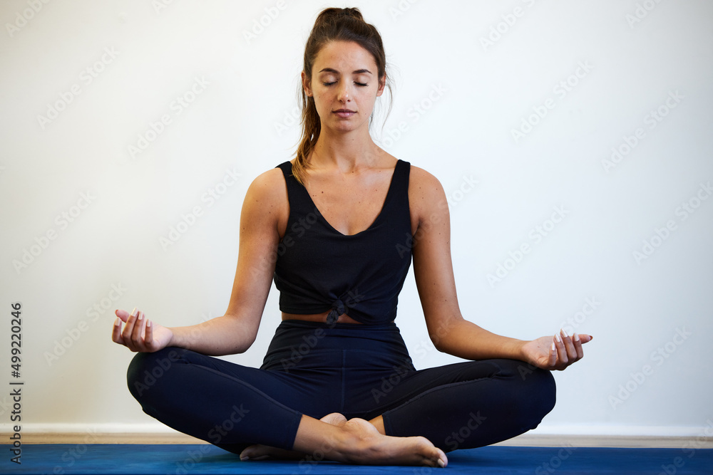 放松你的身体……一张年轻女子坐在家里的瑜伽垫上冥想的照片。