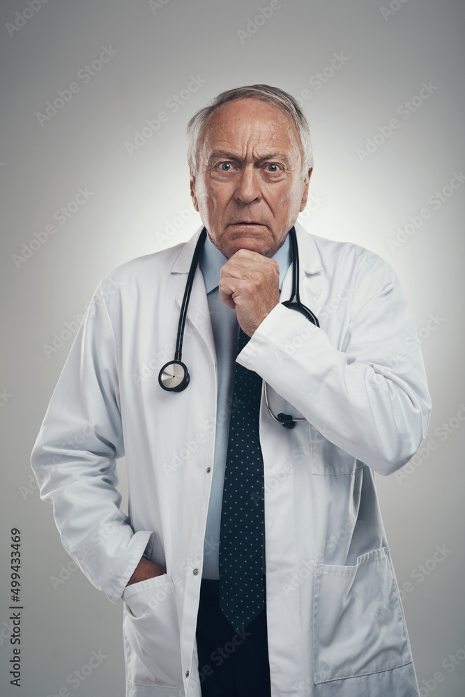 拯救生命是一项严肃的工作。一位年长的男医生在灰色背景下的工作室拍摄