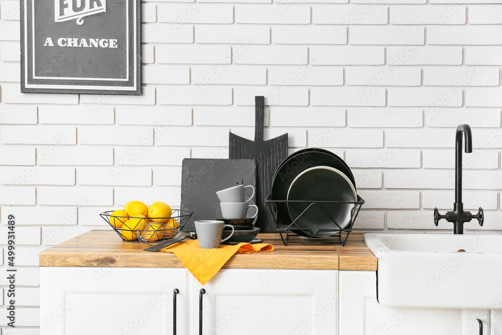 Modern dinnerware and bowl with lemons on counter near white brick wall