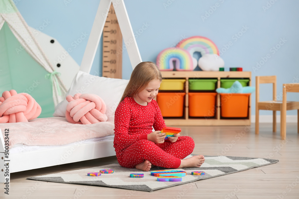 漂亮女孩坐在床边的地板上，在儿童房里玩玩具，坐立不安