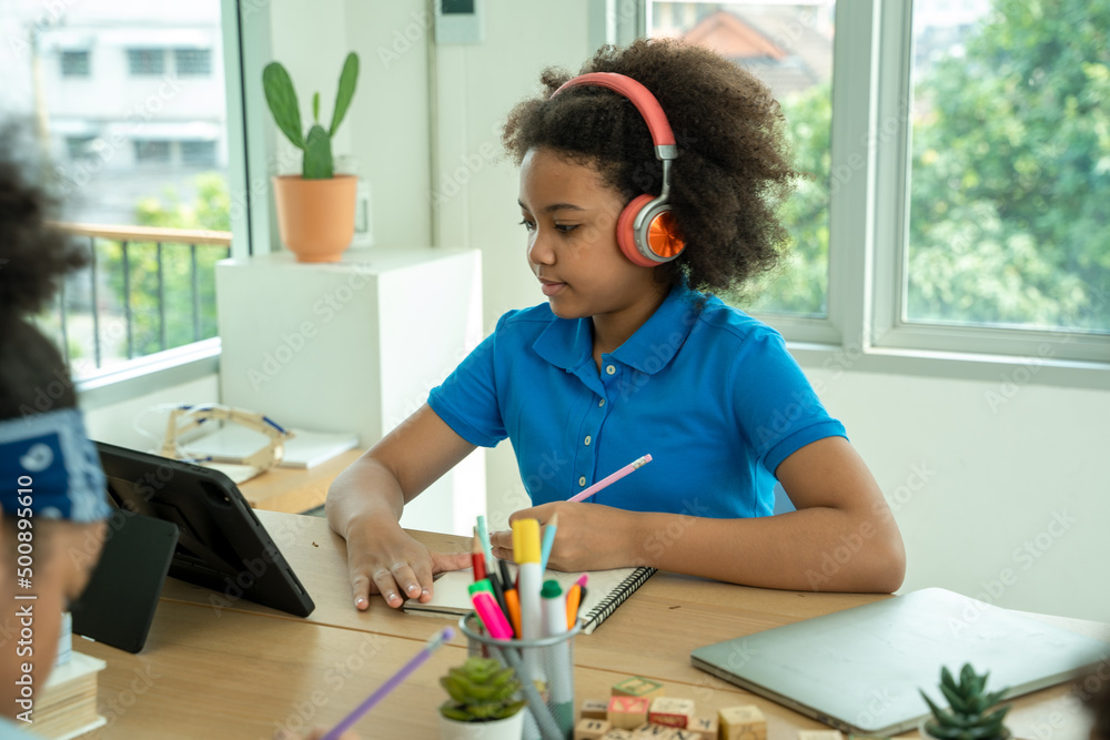 戴着耳机的非裔美国女孩在家里用电脑看视频课，戴着耳机快乐的孩子们
