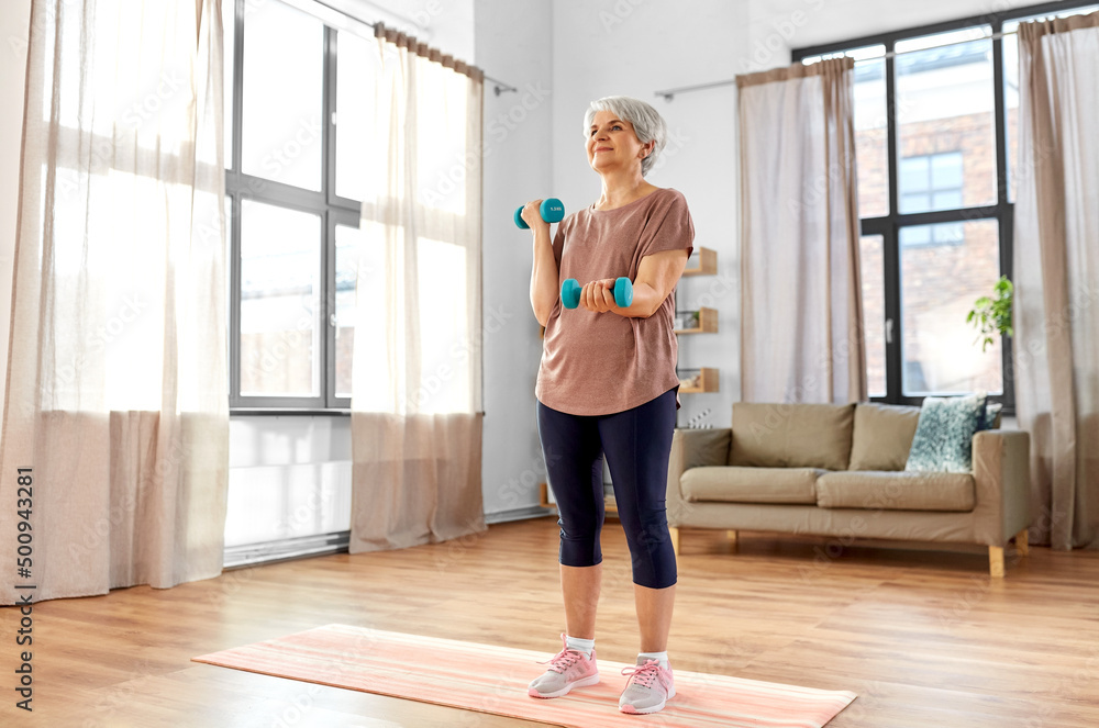 运动、健身和健康的生活方式理念——面带微笑的老年妇女拿着哑铃在垫子上锻炼
