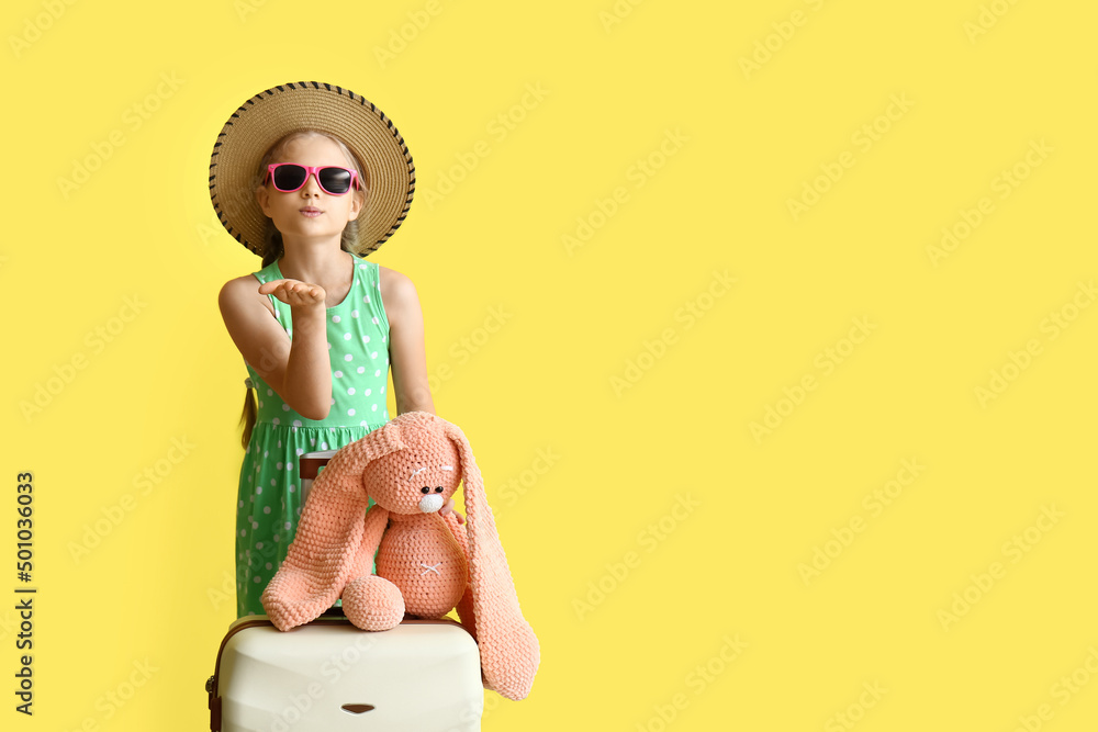 带着行李箱和兔子玩具的可爱小女孩在黄色背景下送上空中之吻