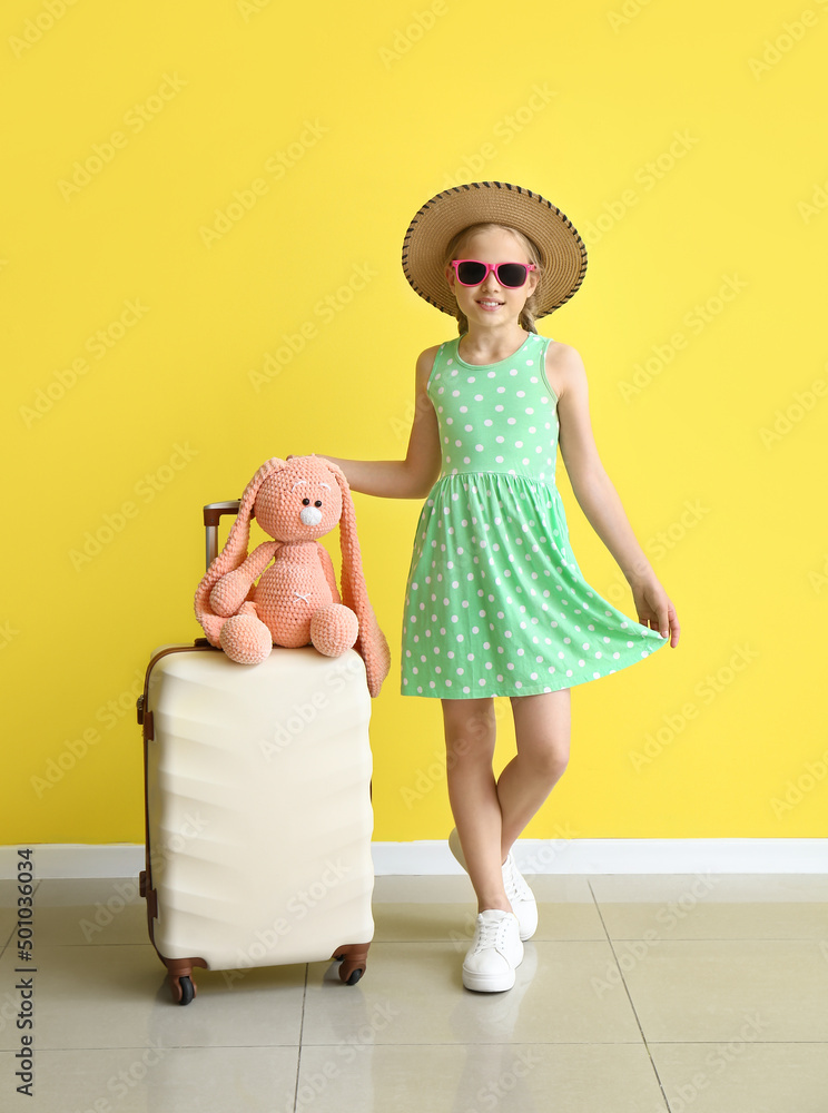 Cute little girl with suitcase and bunny toy near color wall
