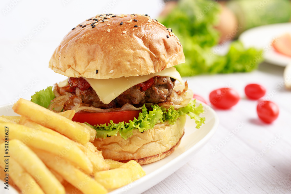 将自制汉堡放在白色桌子上，配薯条、番茄、奶酪、沙拉和牛肉。