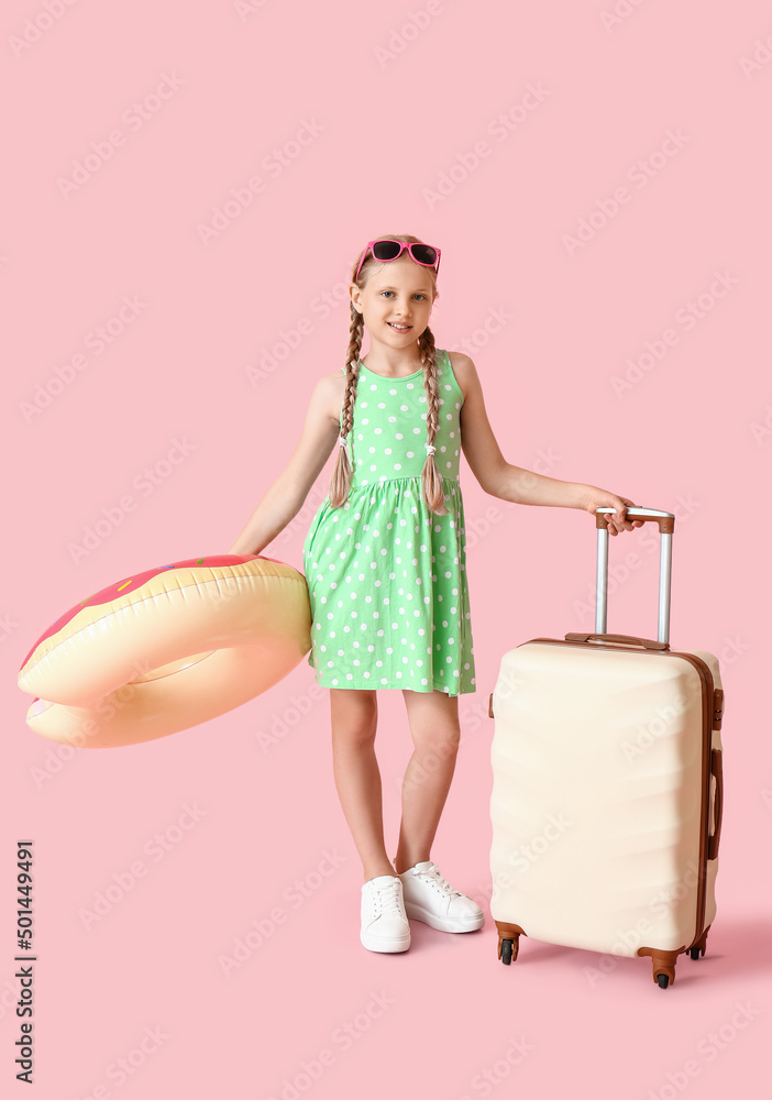 粉色背景带行李箱和充气环的可爱小女孩