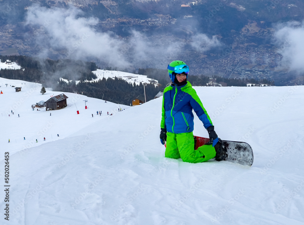 滑雪板上的孩子跪在山上的雪地里