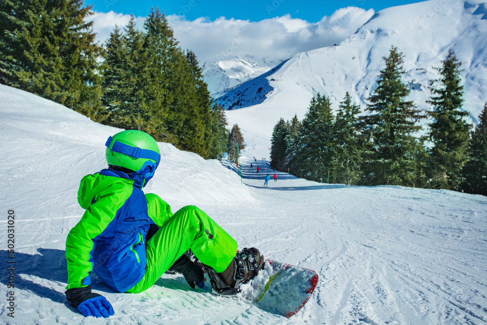 男孩坐在滑雪道上，带着滑雪板向下看