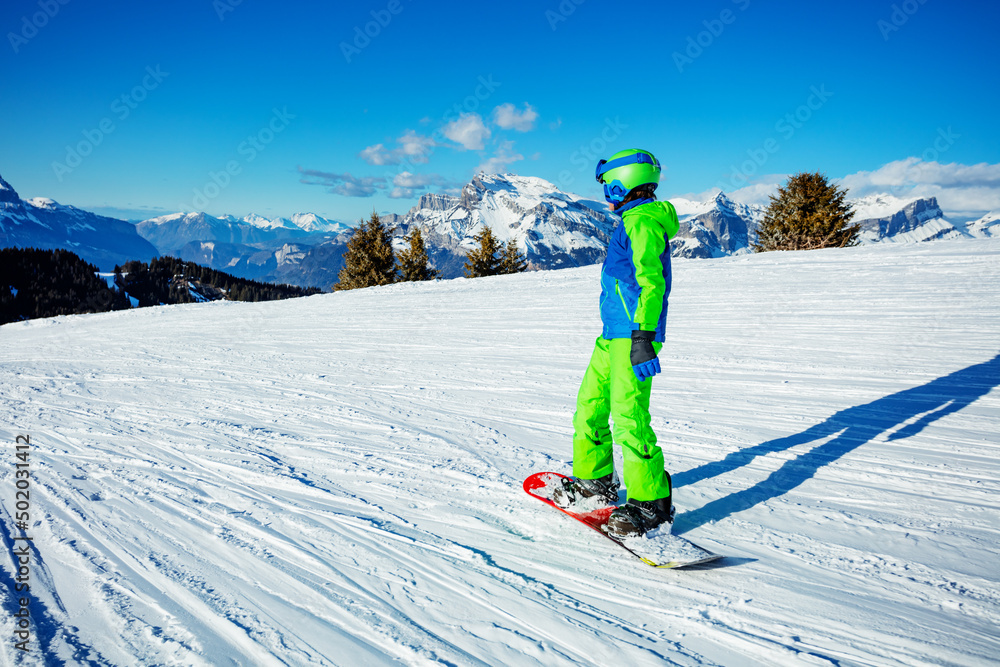 滑雪板上的男孩下坡，身后是壮丽的山脉
