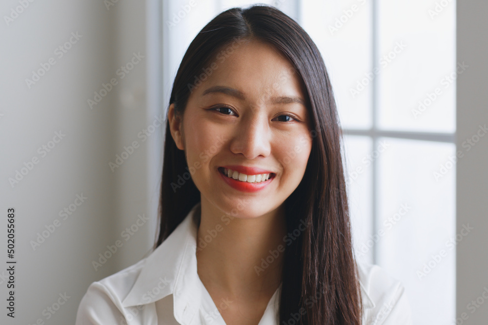 穿着白衬衫在办公室工作的年轻亚洲女商人的肖像，看着相机微笑