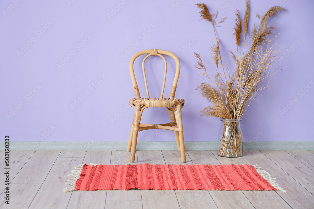房间内部靠近紫色墙壁的带红地毯和花卉装饰花瓶的柳条椅