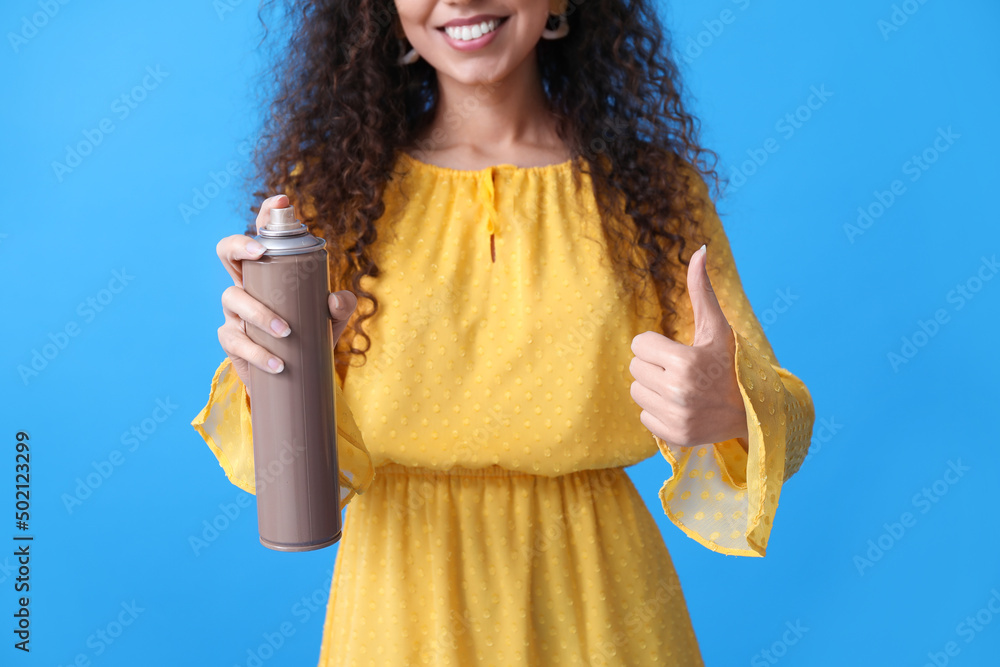 漂亮的年轻非裔美国女人，蓝色背景上喷着发胶，大拇指向上
