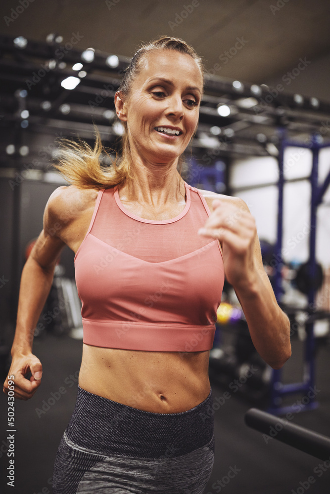 微笑的成熟女人在健身房的跑步机上跑步