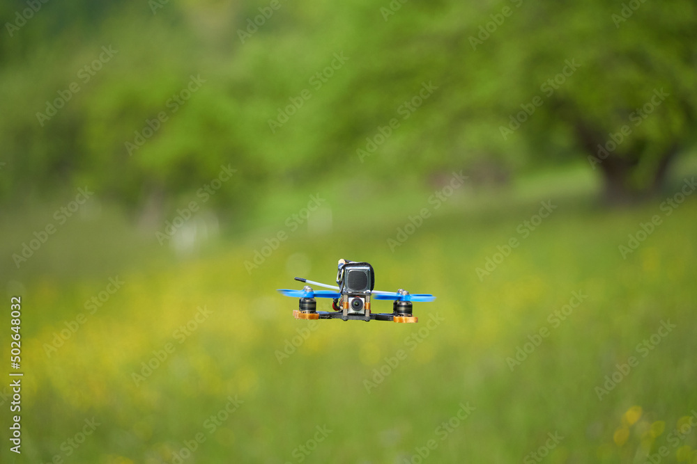 小型赛车直升机也带着蓝色螺旋桨和黑色电池在一片绿色的草地上无人机飞行