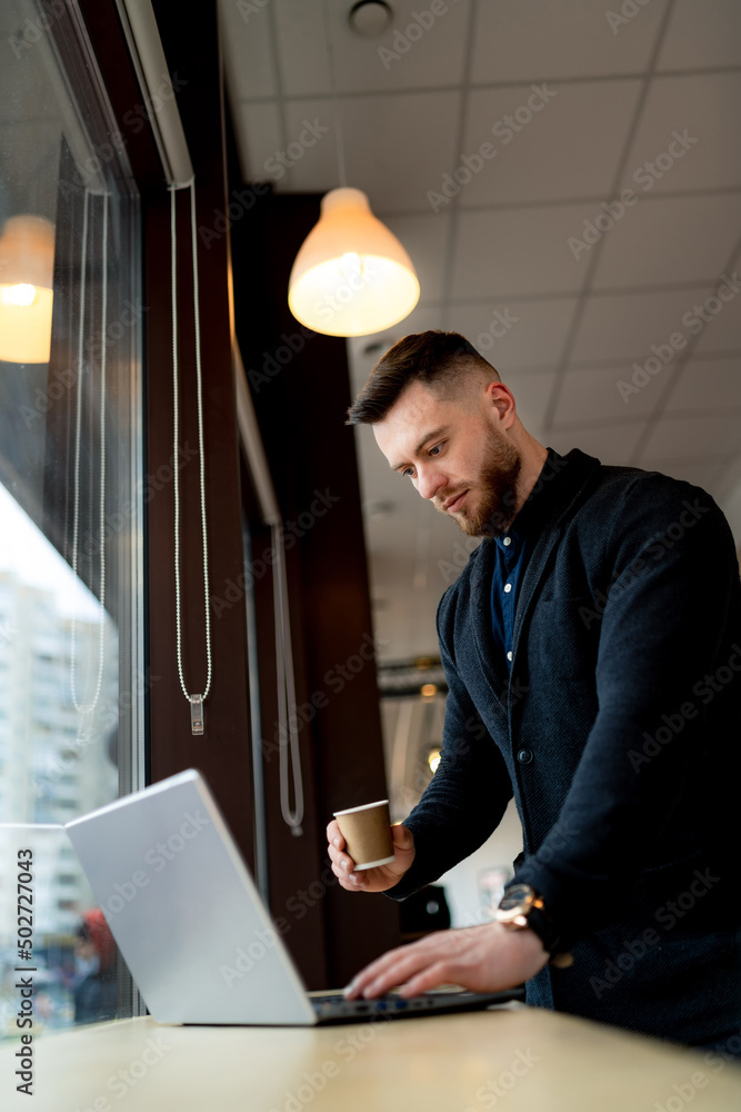 商务人士拿着笔记本电脑喝咖啡休息。咖啡馆里的英俊男子拿着电脑工作。