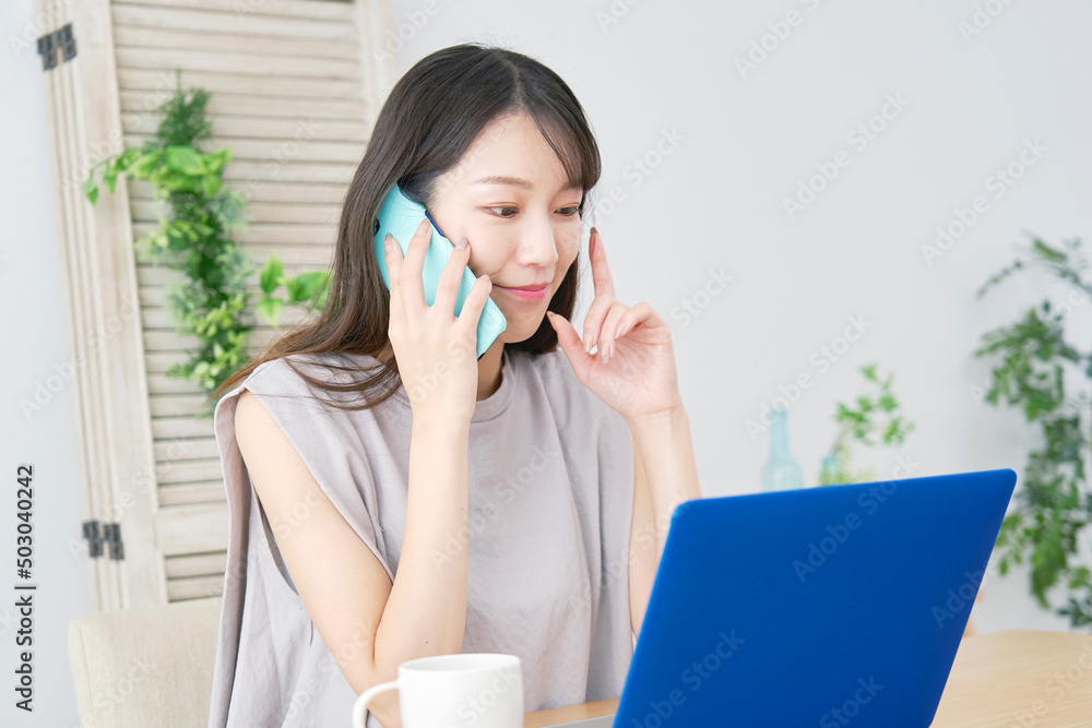 女性　電話をしながらノートパソコンを見る　リビング