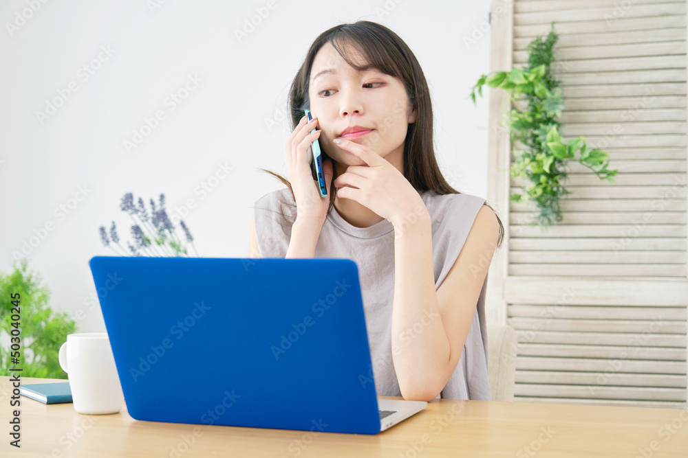 女性　電話をしながらノートパソコンを見る　リビング