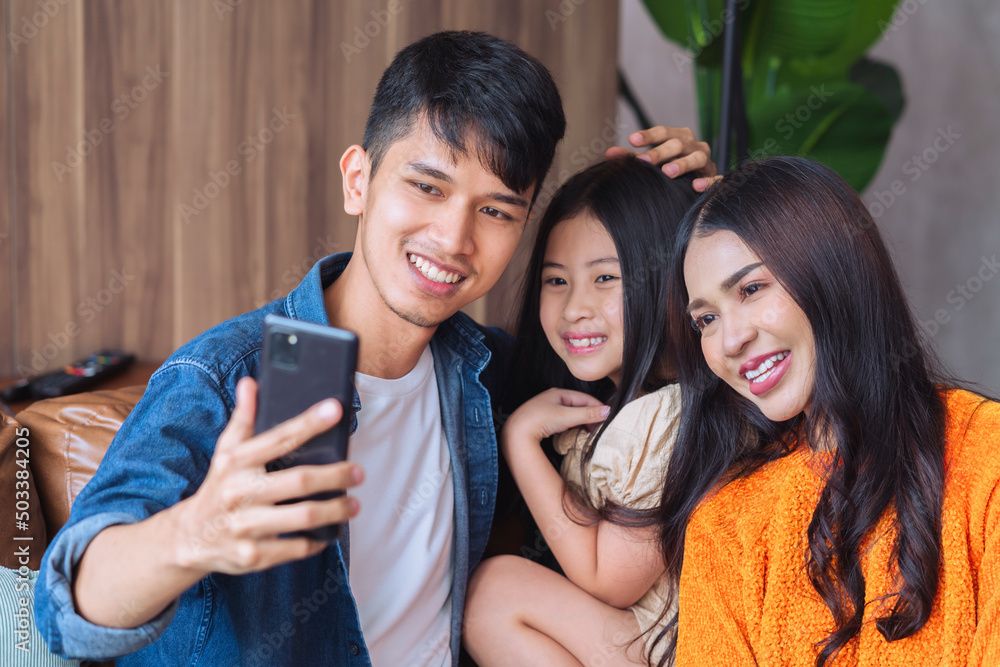 幸福的亚洲家庭呆在家里，使用智能手机自拍或视频通话