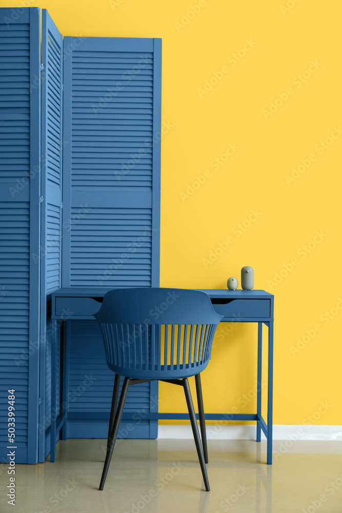 靠近黄色墙壁的蓝色折叠屏幕、桌子和椅子