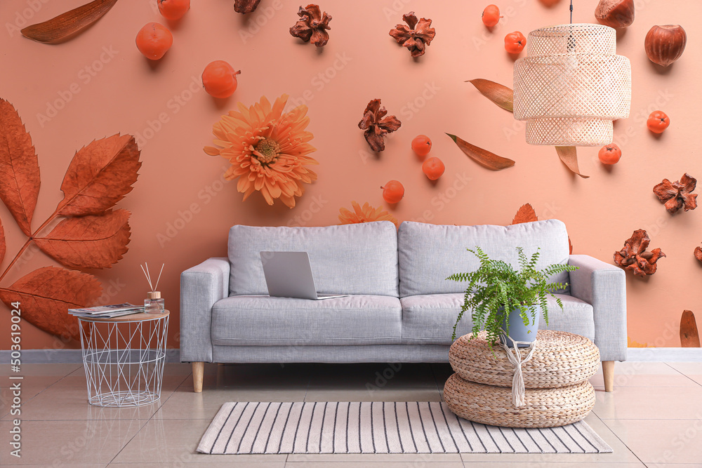 舒适的沙发，配有室内植物和时尚的吊灯，靠近墙壁，带有印花花卉装饰