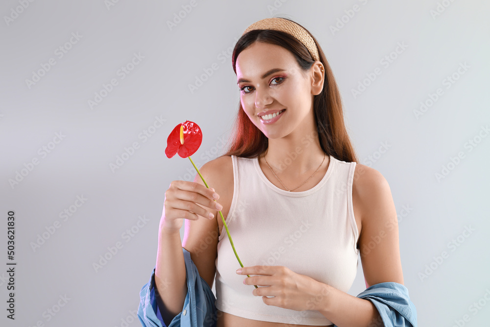 Smiling woman holding anthurium flower on light background