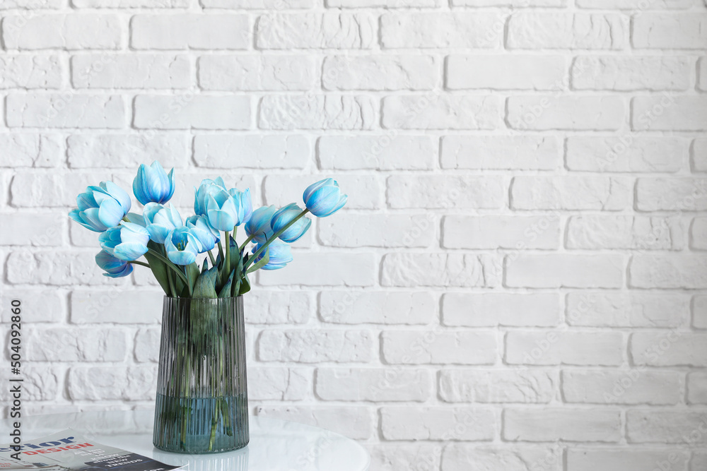 白色砖墙附近的桌子上放着蓝色郁金香和杂志的花瓶