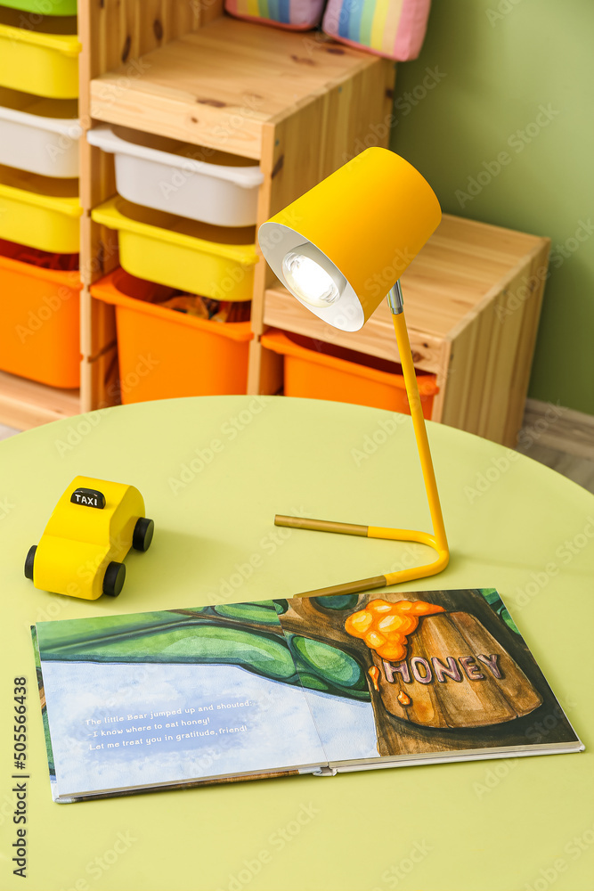 儿童房彩色桌子上的现代灯具、玩具车和书籍
