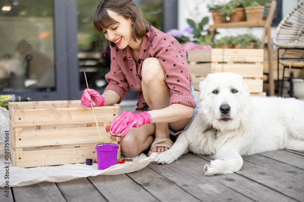 一名年轻女子将木箱漆成粉红色，和她的狗坐在露台上做家务