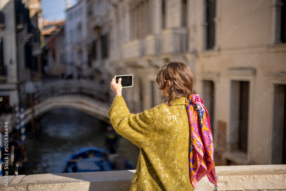 Woman taking photo of beautiful view on venice water canal while traveling in Venice. Woman wearing 