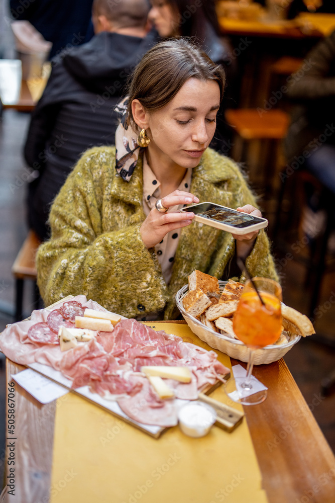女士坐在餐厅里，用意大利肉类开胃菜和雪碧Aperol饮料拍照