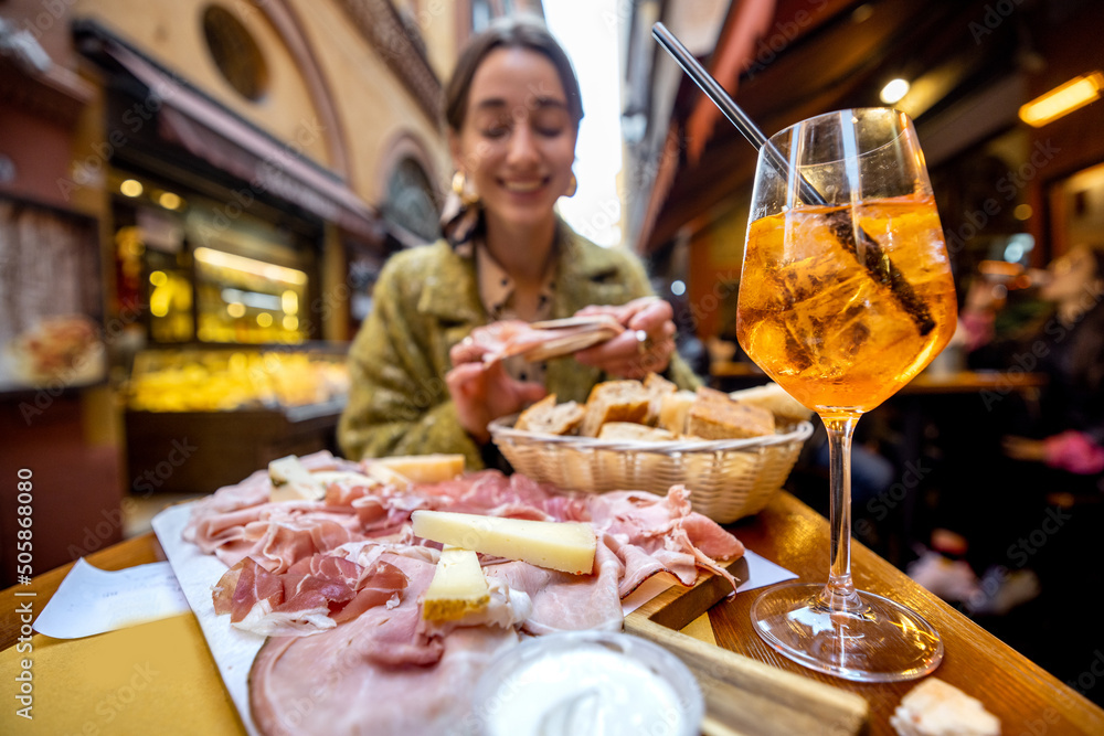 Woman eating italian meat appetizer, various sliced meat and cheese with bread and Aperol Spritz at 