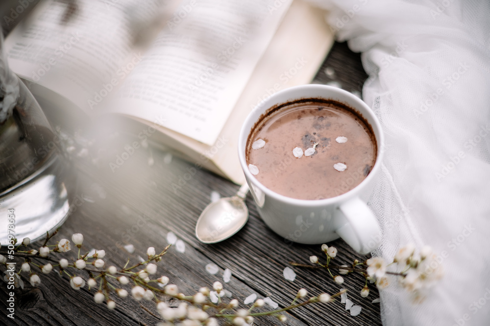 一杯热巧克力可可、旧书和木制背景的春天樱花。阅读概念