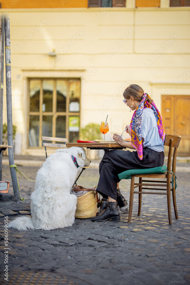 在罗马街头的一家餐厅里，一名妇女和一只狗坐在一起吃意大利意大利面。概念