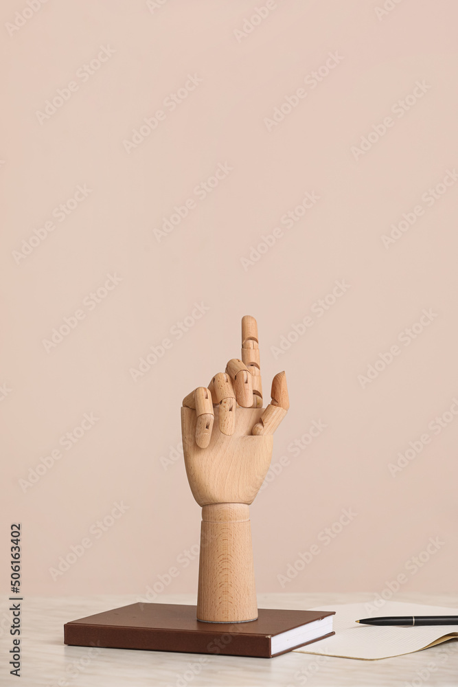 Wooden hand with notebooks on table against beige background
