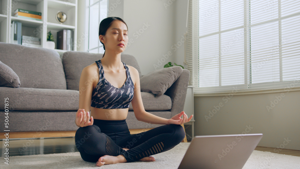 穿着运动服的年轻健康亚洲女性在家里的客厅练习瑜伽，放松身心