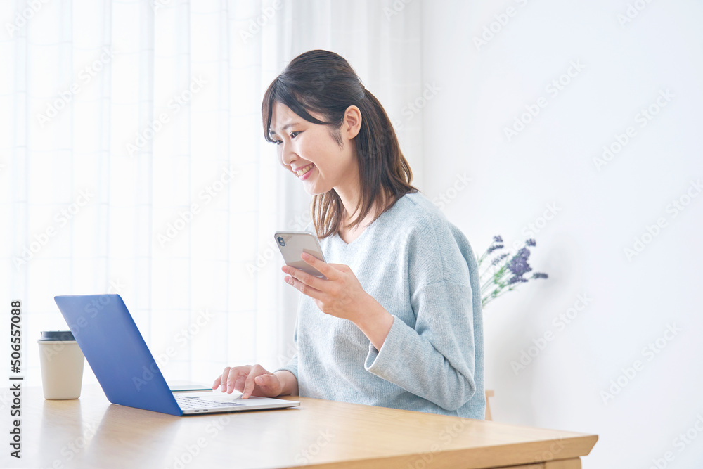 リビングでノートパソコンとスマホを使う女性