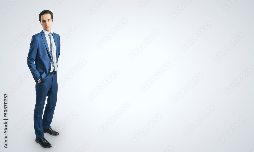 Young confident handsome man in blue suit isolated on blank light grey backgound with empty place fo