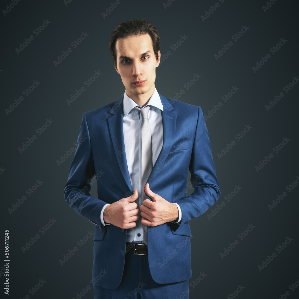 Self-made young businessman in blue suit isolated on abstract dark grey background, closeup