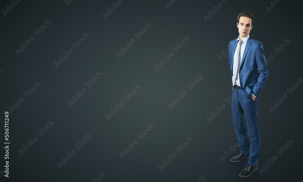 Young confident handsome man in blue suit isolated on blank dark grey backgound with empty place for