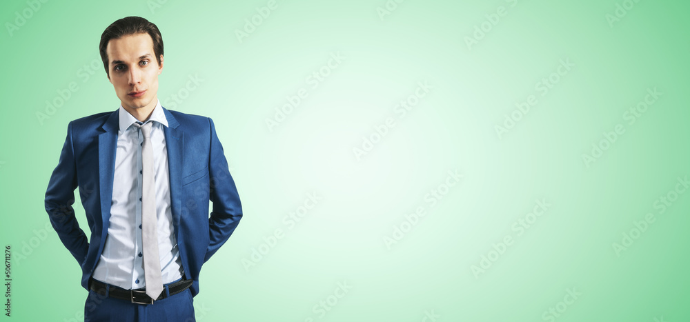 英俊的年轻商人，穿着蓝色西装，隔离在抽象的浅绿色背景上，有文案空间