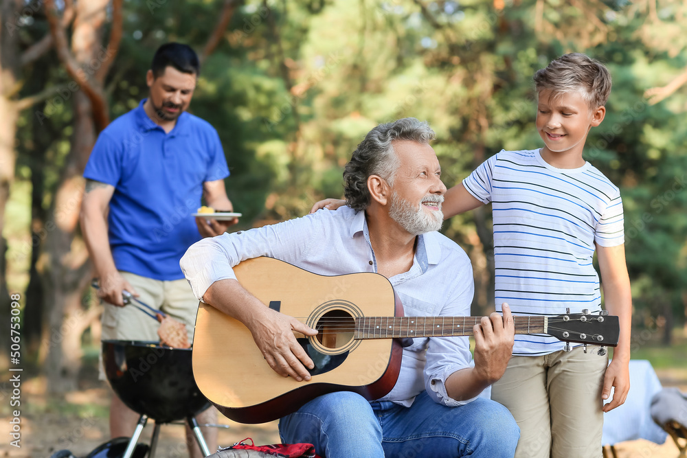 夏日烧烤派对上，一位老人为他的小孙子弹吉他
