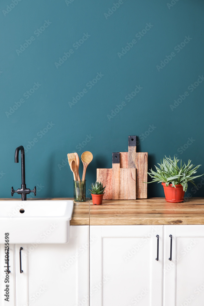 绿色墙壁附近柜台上的木制砧板、抹刀、水槽和室内植物
