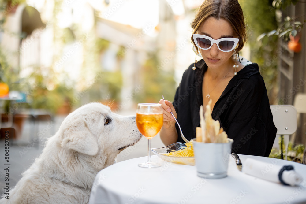 一个女人和她可爱的白狗在户外餐厅吃意大利面。与pe的友谊概念