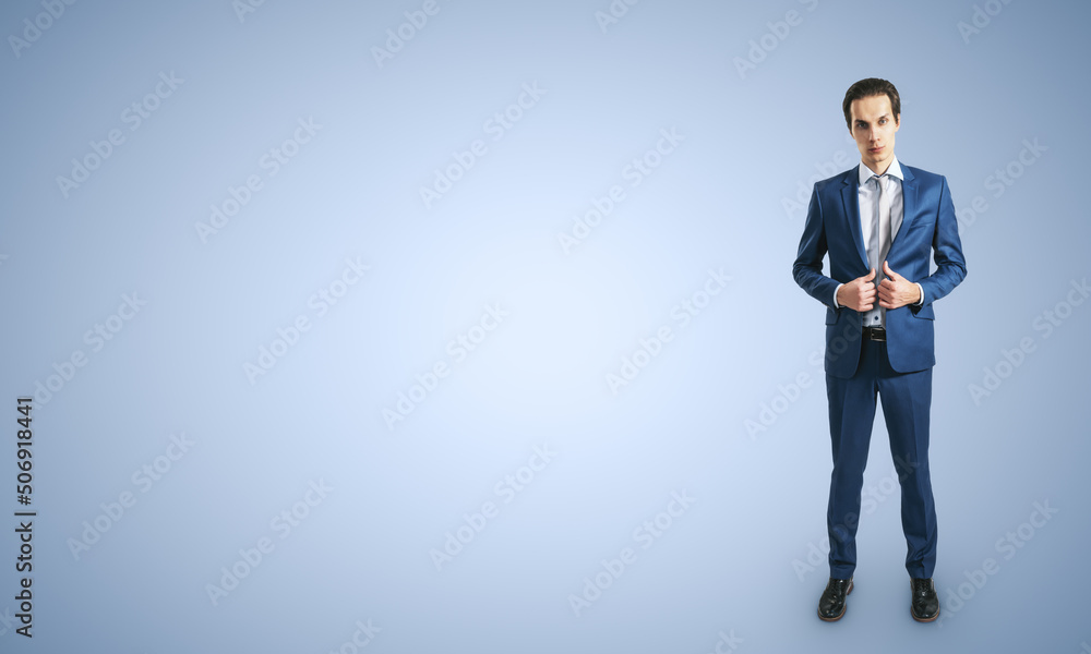 Young self-confident businessman in blue suit and grey tie isolated on light blue wall background wi