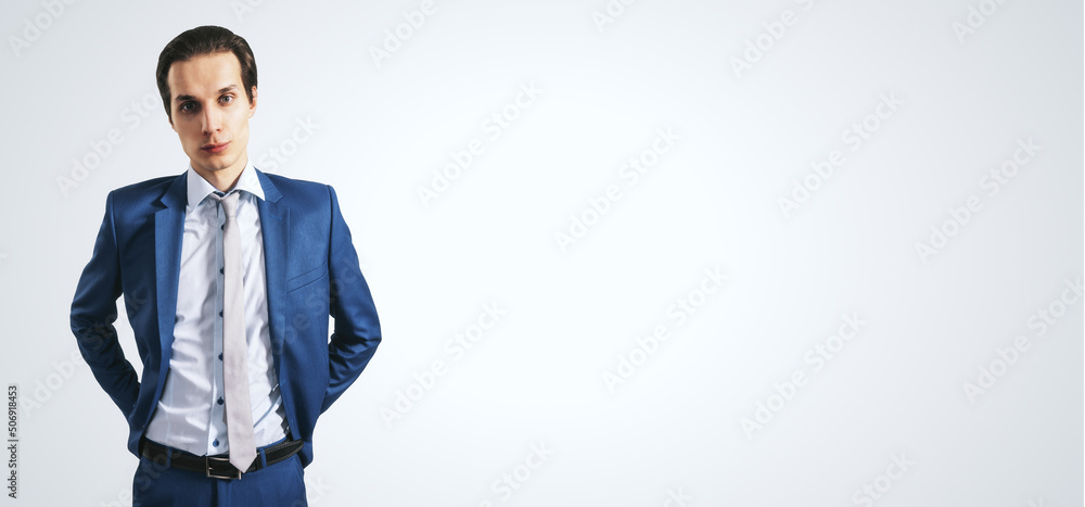 Handsome young businessman in blue suit isolated on abstract light grey backdrop with copyspace for 