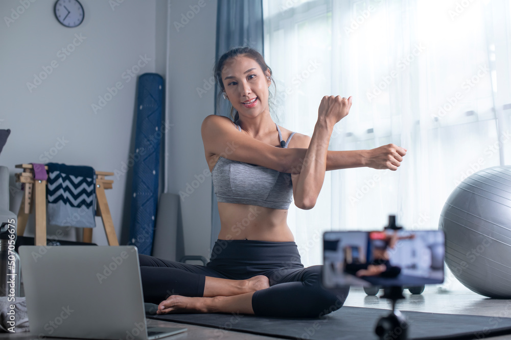 Asian woman using phone camera for live streaming teach yoga online in living room. young female in 