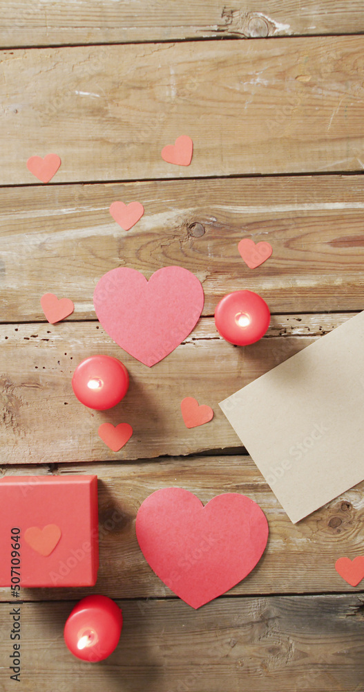 木制桌面上点燃的红色蜡烛、红色心形、礼物和信件的俯视图